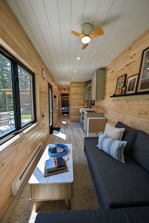 A cabin interior with a wooden interior, a sofa, a coffee table, a ceiling fan, and a kitchen area.