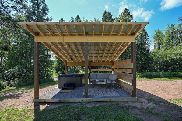 A covered outdoor seating area with a hot tub and a sofa.