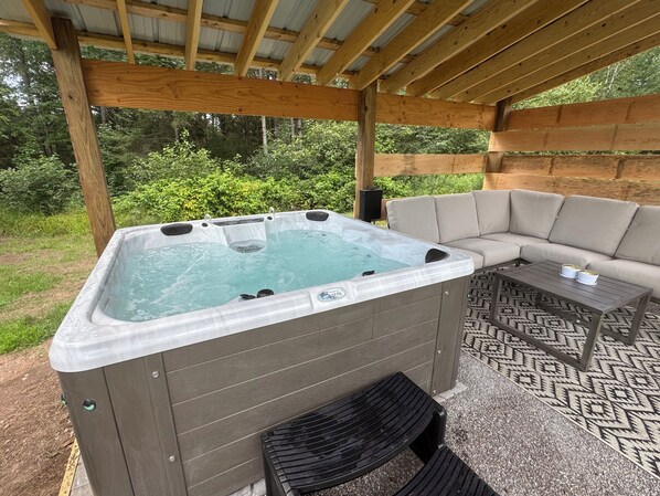 Een hottub onder een houten pergola met een beige bank en een tafel met dessin in de buurt.