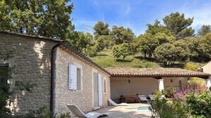 Un bâtiment en pierre avec un toit en tuiles, un espace piscine avec des chaises longues et un jardin agrémenté de différentes plantes.