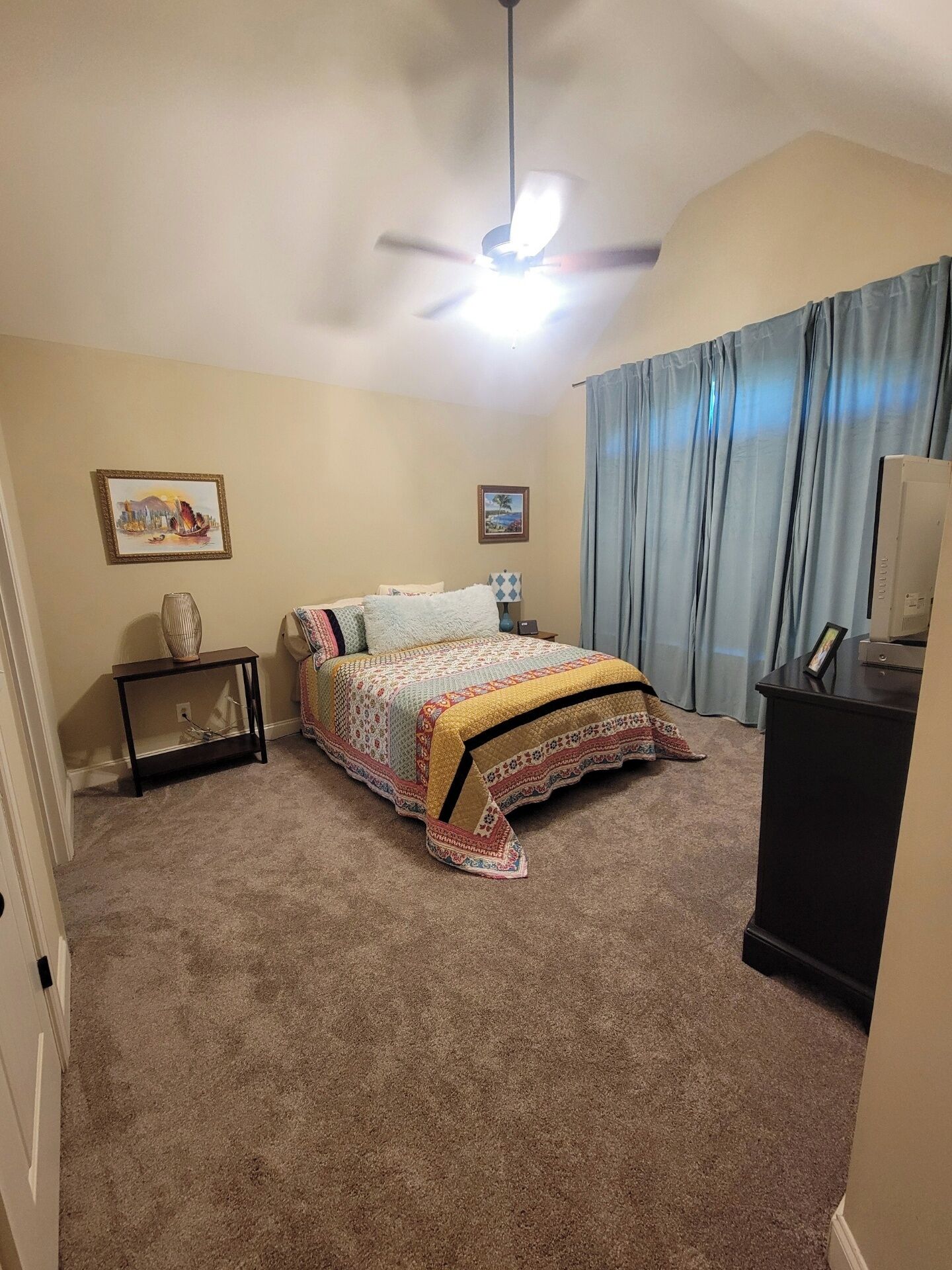 Ein Schlafzimmer mit Bett, Deckenventilator, Schreibtisch und Fernseher.