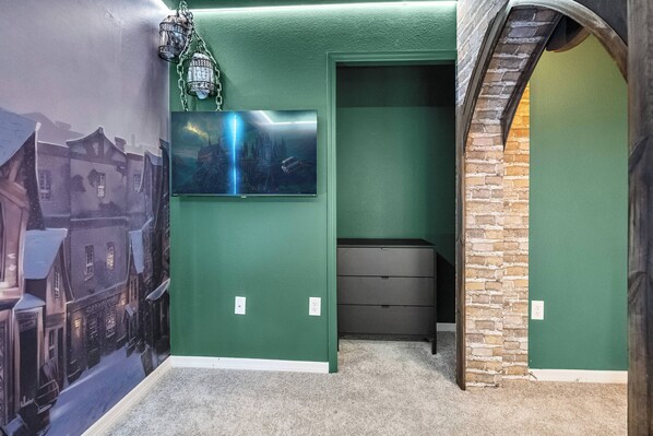 A room with green walls, a stone accent wall, a flat-screen TV mounted above a dresser, and a mural of a snowy street scene.