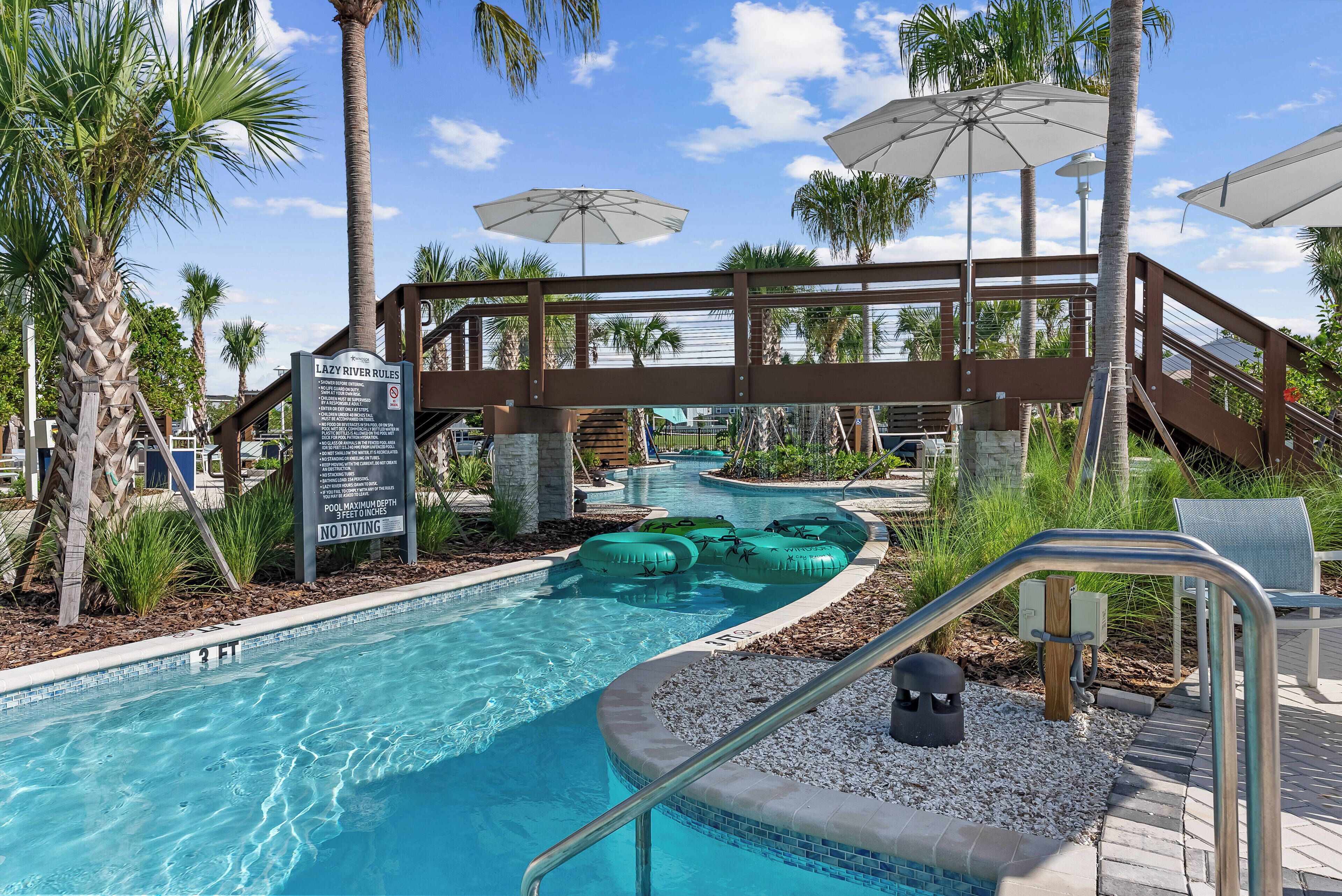 A pool area with a lazy river, palm trees, and umbrellas.