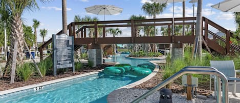 A pool area with a lazy river, palm trees, and umbrellas.
