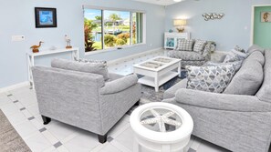 Bright living room with coastal accents, comfortable sofas, and views of the tropical greenery outside.