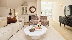 Un salon moderne avec un canapé blanc, des fauteuils à motifs, une table basse, une cheminée et un téléviseur.
