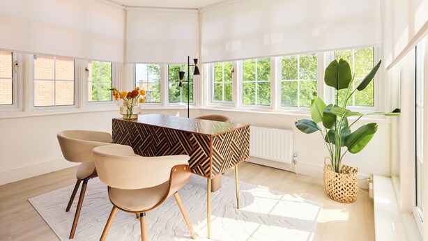 Un espace repas moderne avec une table et des chaises en bois, de grandes fenêtres et une plante en pot.
