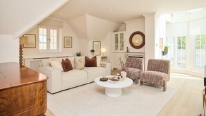 Un salon spacieux avec un plafond haut, un canapé blanc, une table basse et un fauteuil à motifs.