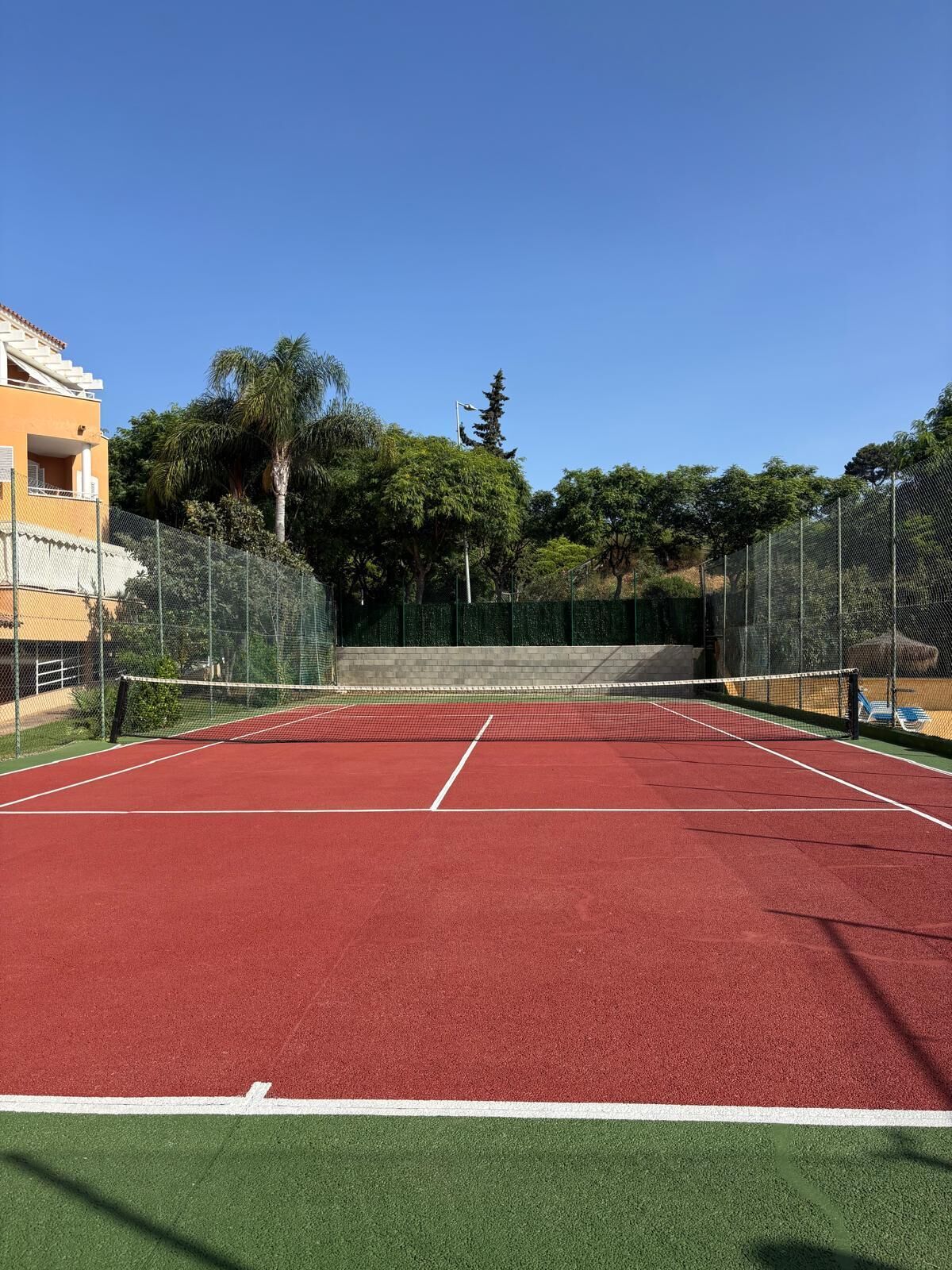 Una cancha de tenis con una red, rodeada por una valla y árboles.