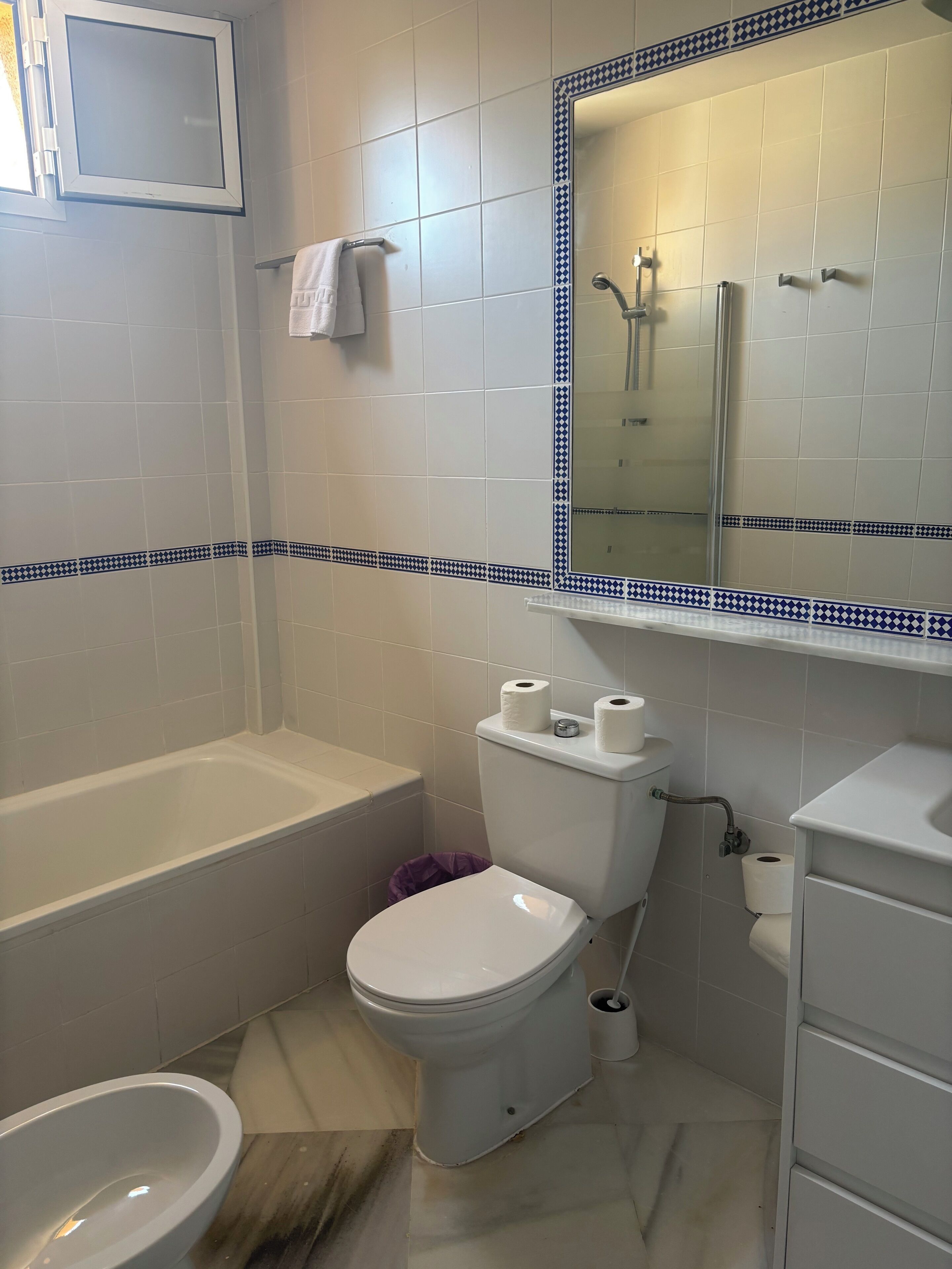Une salle de bain équipée d’une baignoire, de toilettes, d’un bidet et d’un miroir orné d’un cadre décoratif.