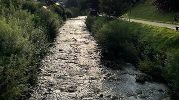 Een rivier die door een vallei stroomt, met huizen aan de ene kant en een weg aan de andere kant, onder een gedeeltelijk bewolkte lucht.