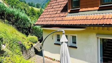 Ein zweistöckiges Haus mit rotem Ziegeldach, einer kleinen Veranda mit weißem Sonnenschirm und einem gepflegten Garten.