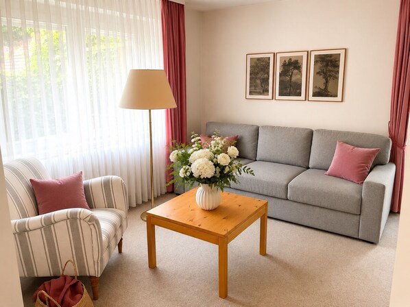 A living room with a sofa, a striped armchair, a wooden coffee table, and a vase of flowers. - Ferienhaus Oesterle - Idyllic Black Forest house by a stream with terrace & balcony (Baiersbronn (Schönmünzach))