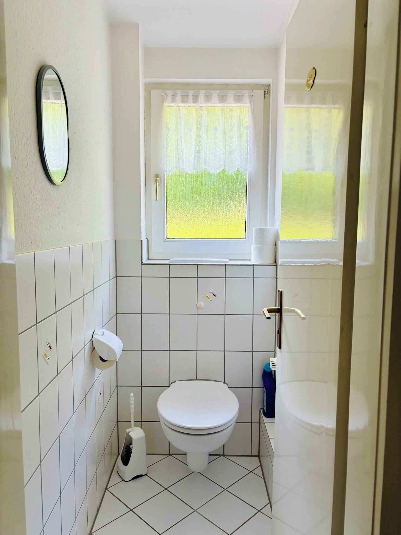 A small bathroom with a toilet, a hand dryer, and a window with a curtain.