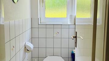 A small bathroom with a toilet, a hand dryer, and a window with a curtain.
