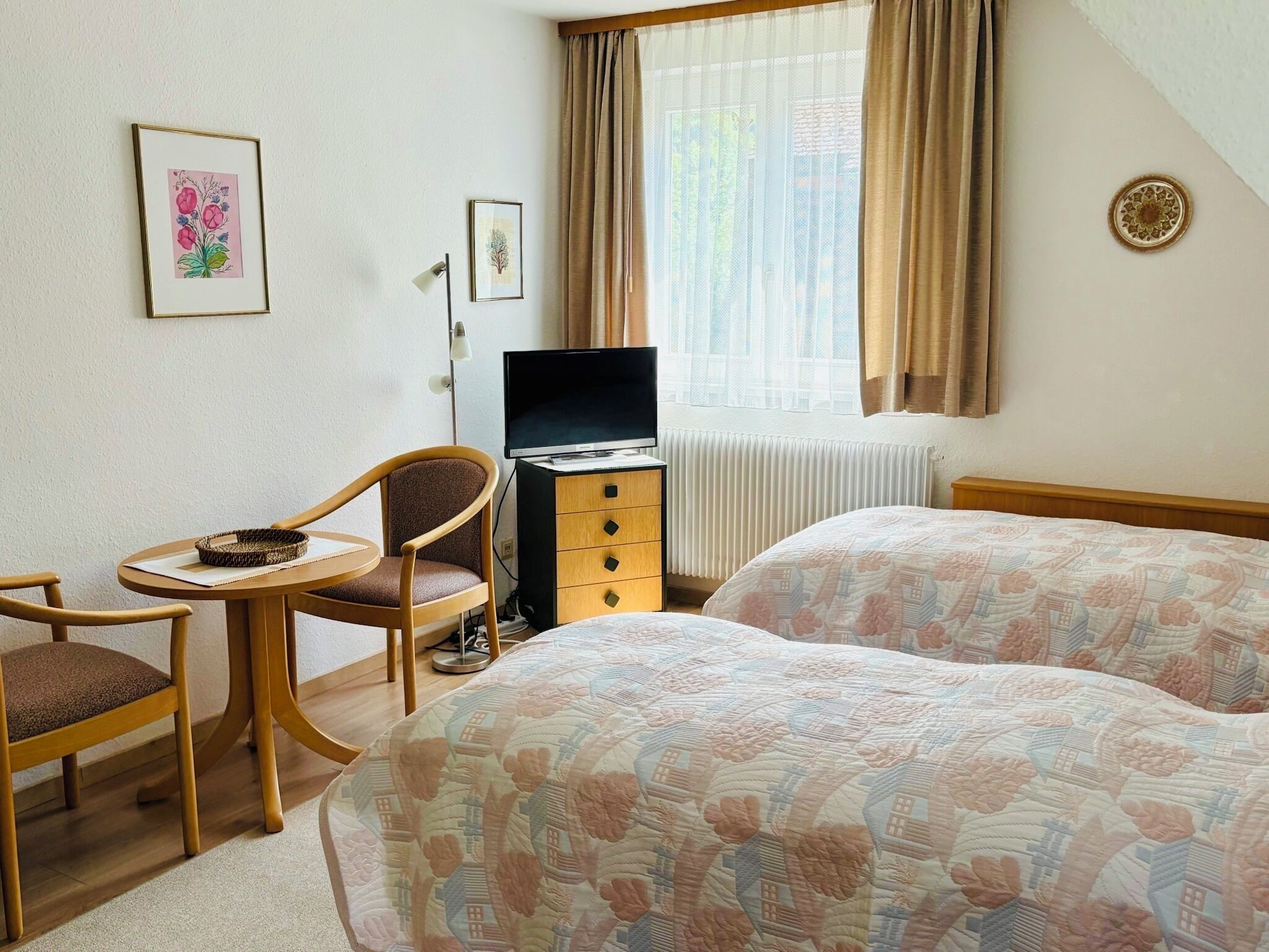 A hotel room with two beds, a desk with a chair, a television, and a window with curtains.