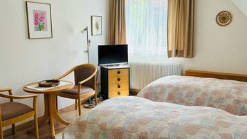 A hotel room with two beds, a desk with a chair, a television, and a window with curtains.