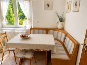 Un coin repas avec une table, des chaises et un banc. Un saladier rempli de fruits est posé sur la table.