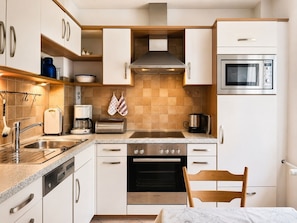 Une cuisine moderne avec des meubles blancs, des appareils en acier inoxydable, un four Bosch et un four à micro-ondes.