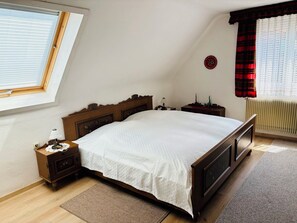 A bedroom with a wooden bed, a nightstand, a lamp, a radiator, and a window with curtains. - Ferienhaus Oesterle - Idyllic Black Forest house by a stream with terrace & balcony (Baiersbronn (Schönmünzach))