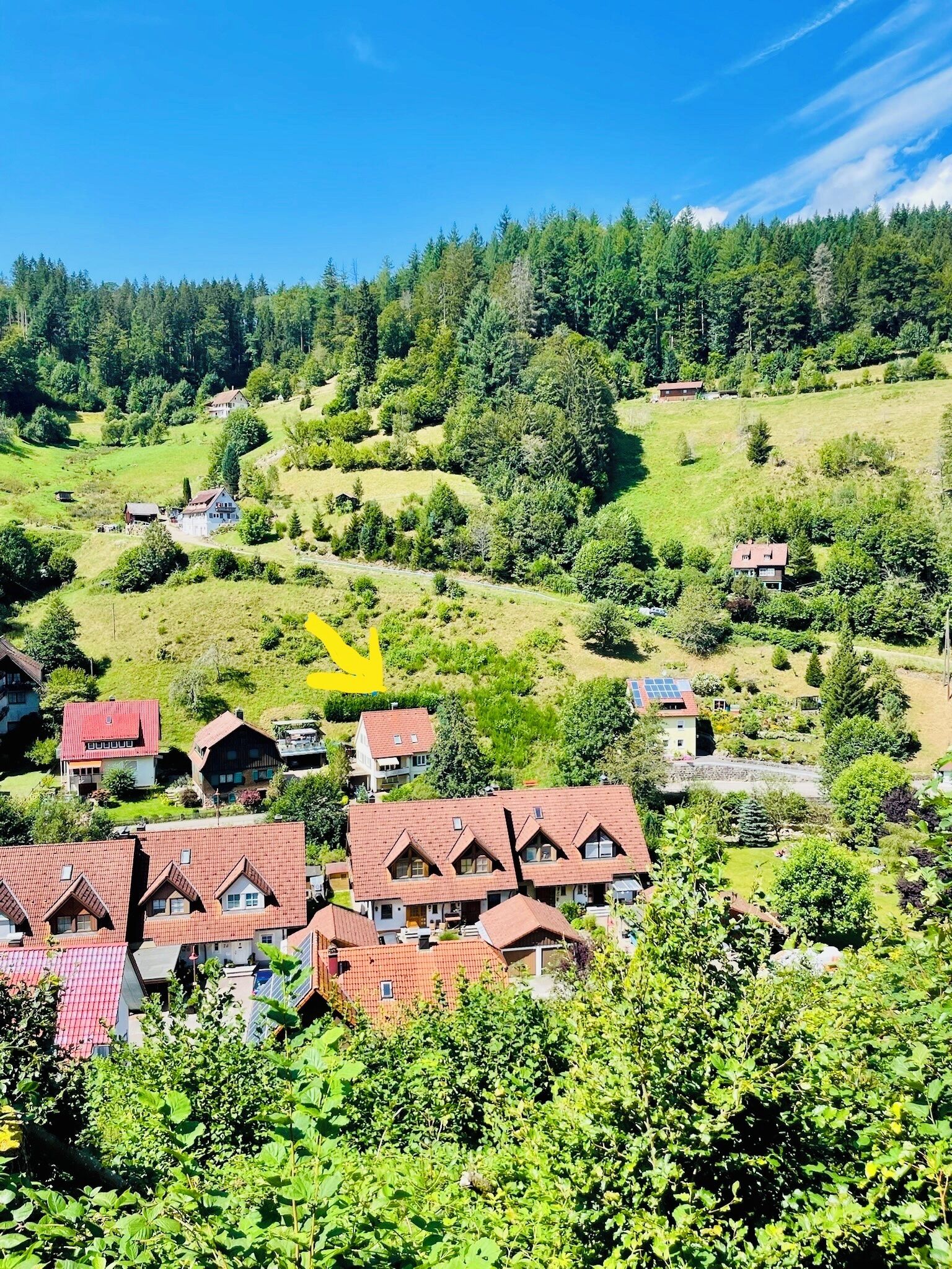 A hillside village with traditional red-roofed houses, a clear blue sky, and a yellow arrow pointing to a specific location.