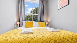 Ein Hotelzimmer mit einem großen Bett, zwei Kissen, einem Fenster mit Vorhängen und einem gerahmten Bild an der Wand.
