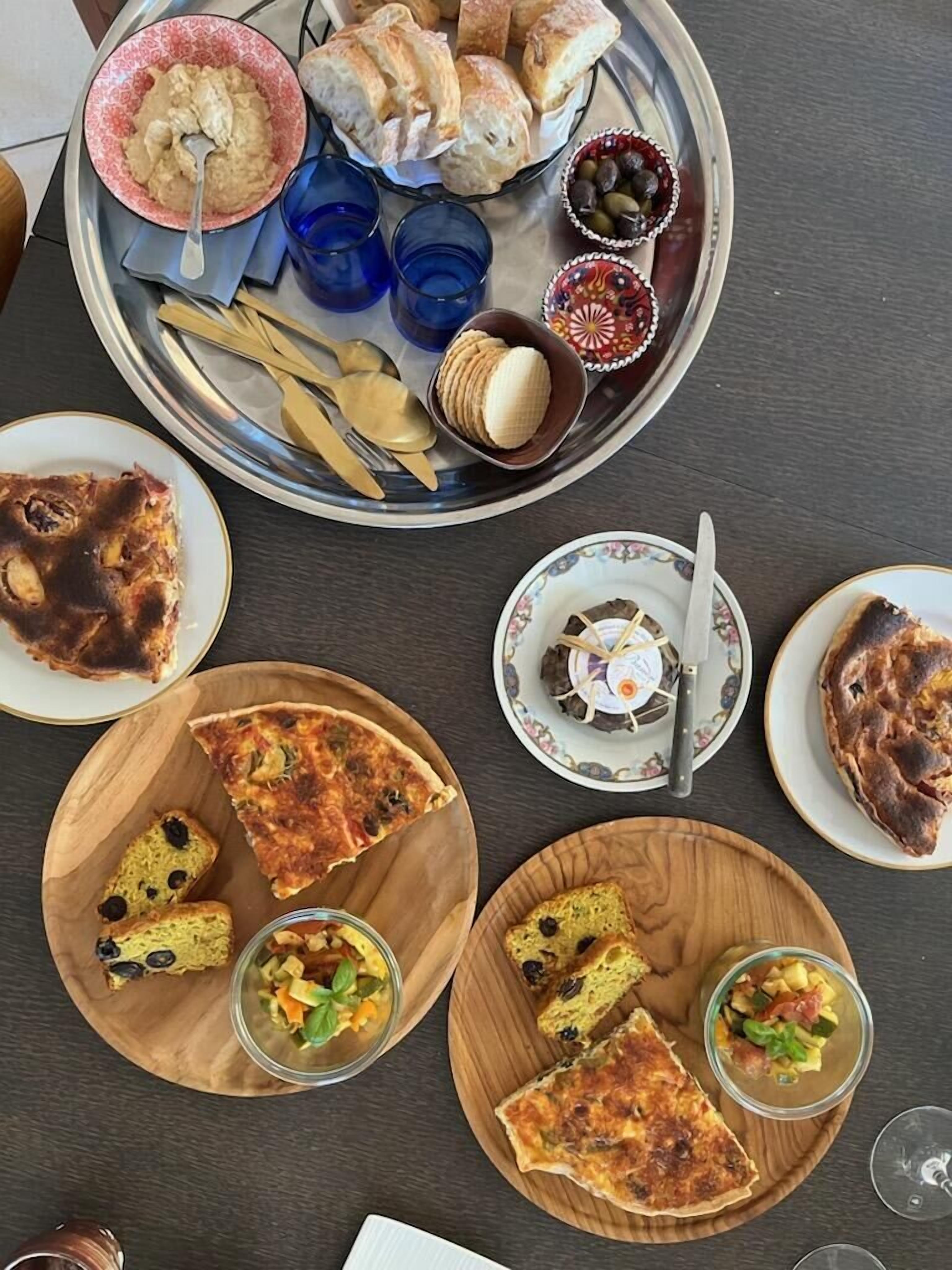 Une table avec divers plats, notamment des pizzas, du pain, et un plateau contenant des petits pains et des olives.