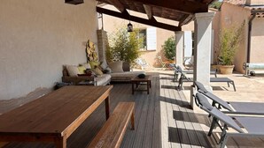 Un patio al aire libre con mobiliario de madera, que incluye una mesa y bancos, y una zona cubierta con una pérgola.