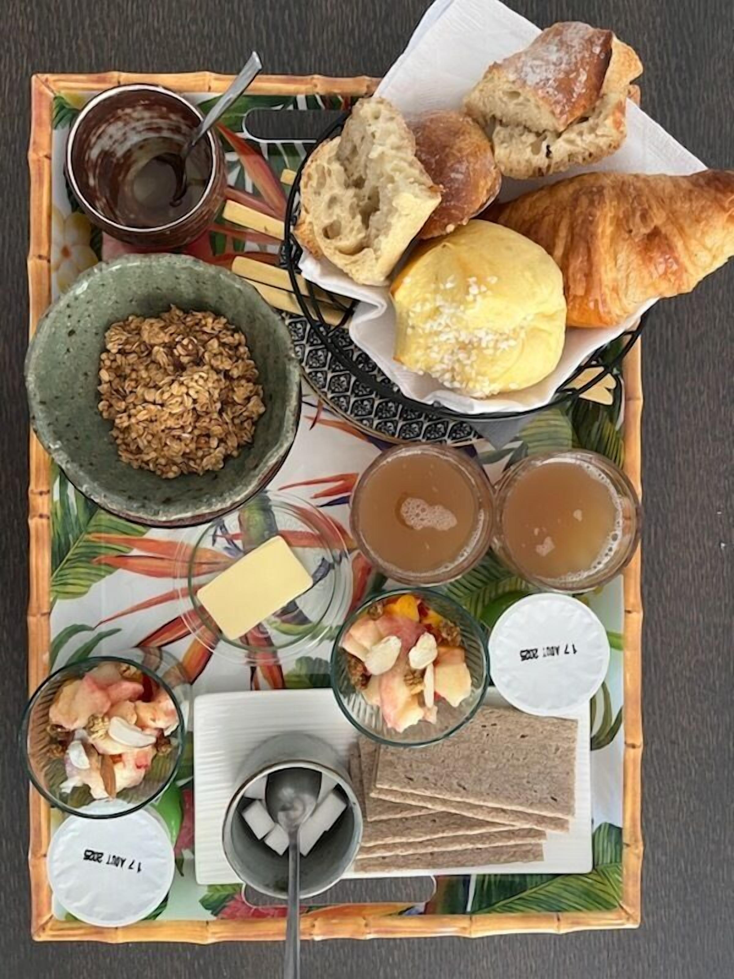 A tray with various food items including bread, pastries, and a bowl of granola.