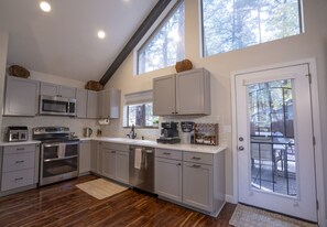 A modern kitchen with grey cabinets, stainless steel appliances, and a large window providing natural light.