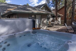 Un jacuzzi en un patio trasero con un porche cubierto y mobiliario exterior.