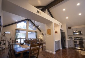 A spacious kitchen with modern appliances, a dining area with a large table and chairs, and a high ceiling with exposed beams.