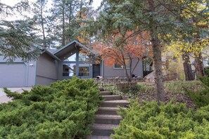 Ein modernes Haus mit einer Steinstufe, die zum Eingang führt, umgeben von dichtem Grün und Bäumen mit Herbstlaub.