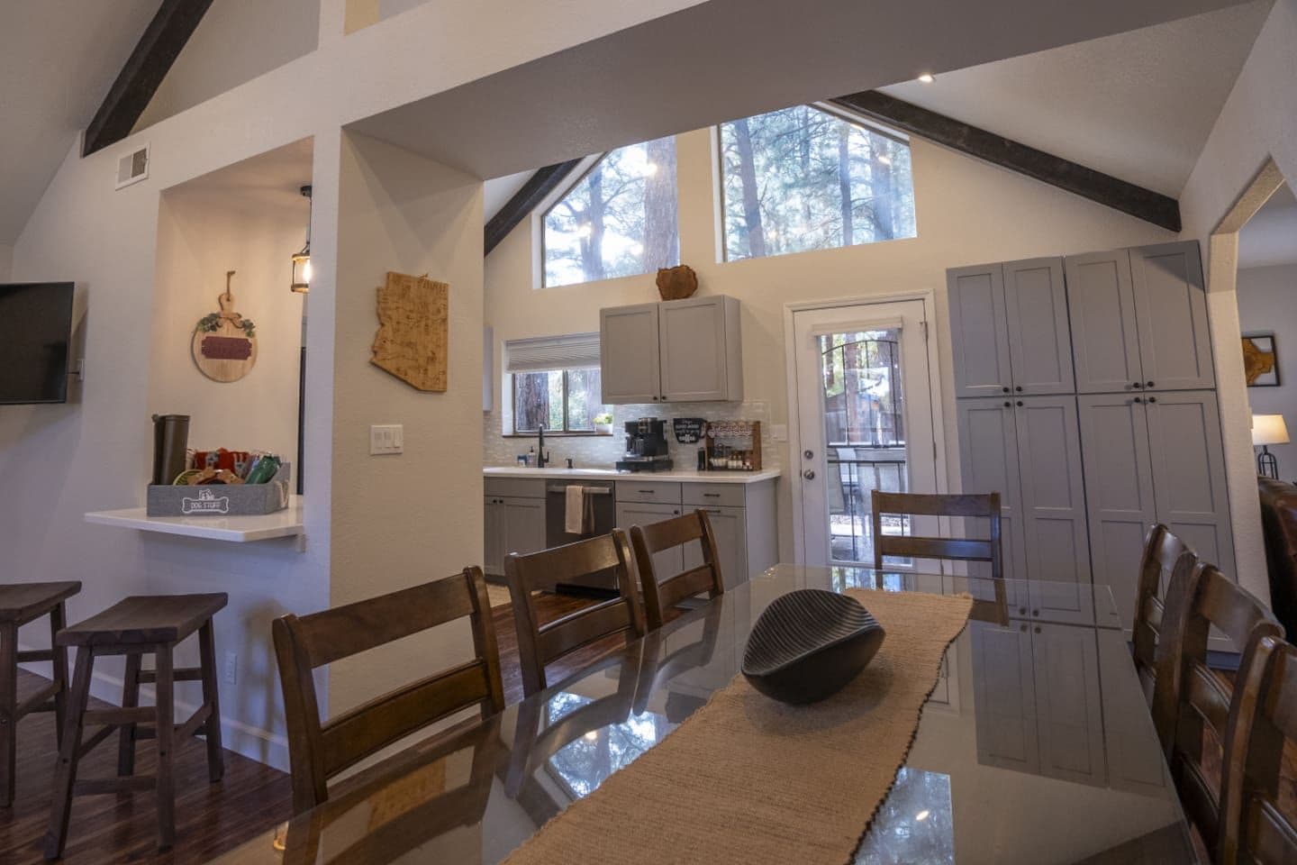 Uma sala de jantar com mesa de vidro, cadeiras de madeira e uma cozinha ao fundo.