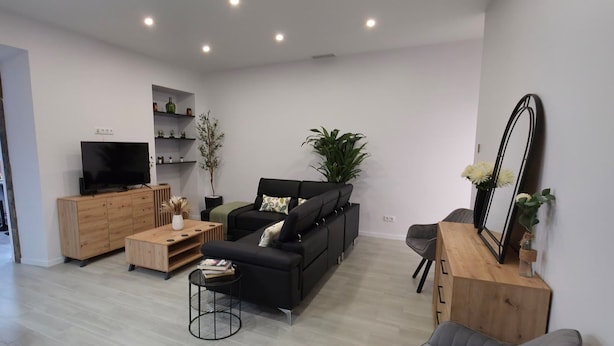 Un salón moderno con un sofá negro, un aparador de madera y un televisor sobre un mueble de madera.