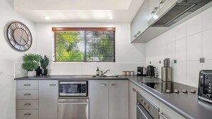 Une cuisine moderne dotée d’appareils électroménagers en acier inoxydable, d’un four encastré et d’une fenêtre avec des stores.