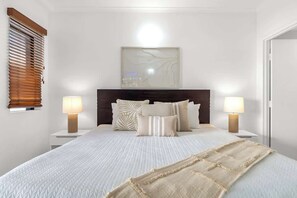 Une chambre à coucher bien aménagée, avec un grand lit, deux tables de chevet avec des lampes, une tête de lit et une œuvre d’art accrochée au mur.