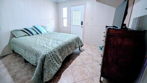 Ein Schlafzimmer mit Bett, Kommode, Tür und Fenster.