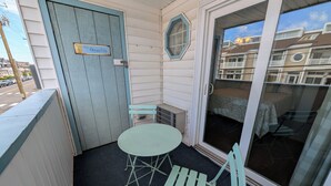A small balcony with a table and chairs, a door labeled 'Ocean City,' and a view of a residential building. - Beach block condo minutes to the boardwalk in Ocean City - Perfect for a getaway (Ocean City)