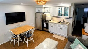 A compact kitchen with white cabinets, a stainless steel refrigerator, a stove, and a flat-screen TV mounted on the wall. - Beach block condo minutes to the boardwalk in Ocean City - Perfect for a getaway (Ocean City)