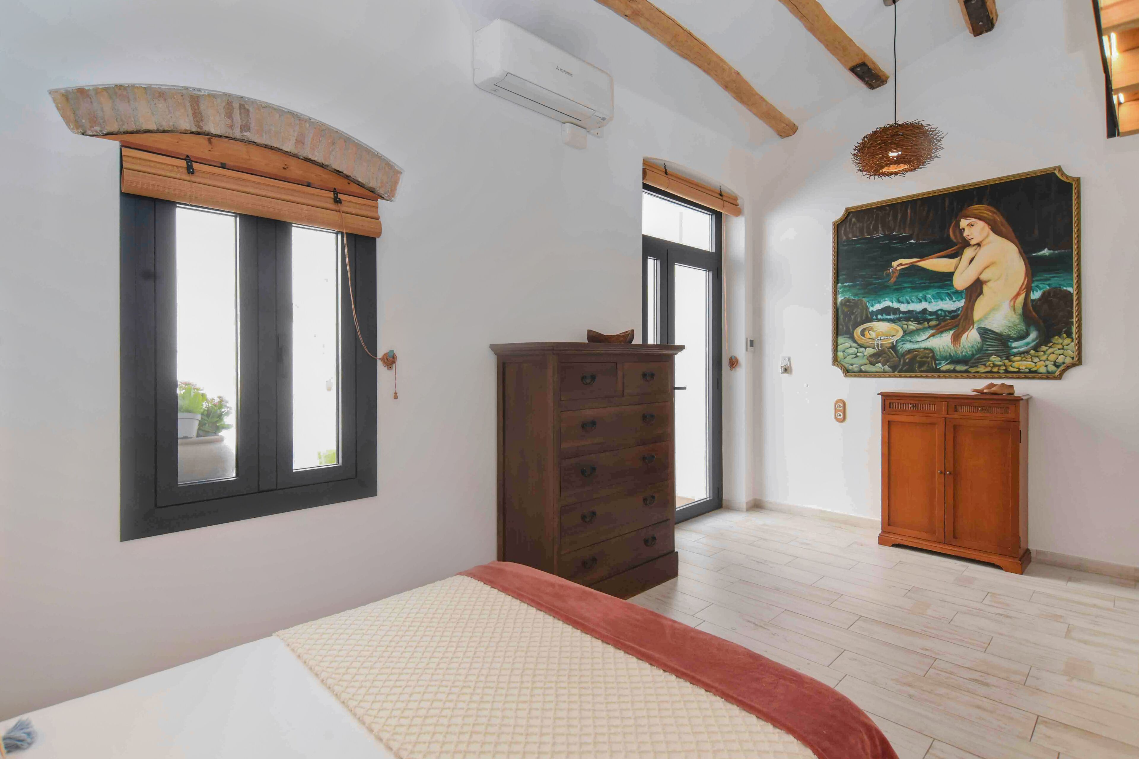 Un dormitorio con una cama, un aparador de madera, un cuadro y una ventana.