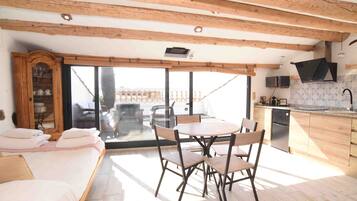 Una cocina moderna con vigas de madera, una zona de comedor con mesa y sillas, horno empotrado y un gran ventanal corredero que da a un patio exterior.