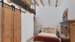 Un dormitorio con un armario de madera, una cama con una colcha roja, un tocador y una escalera con vigas de madera.