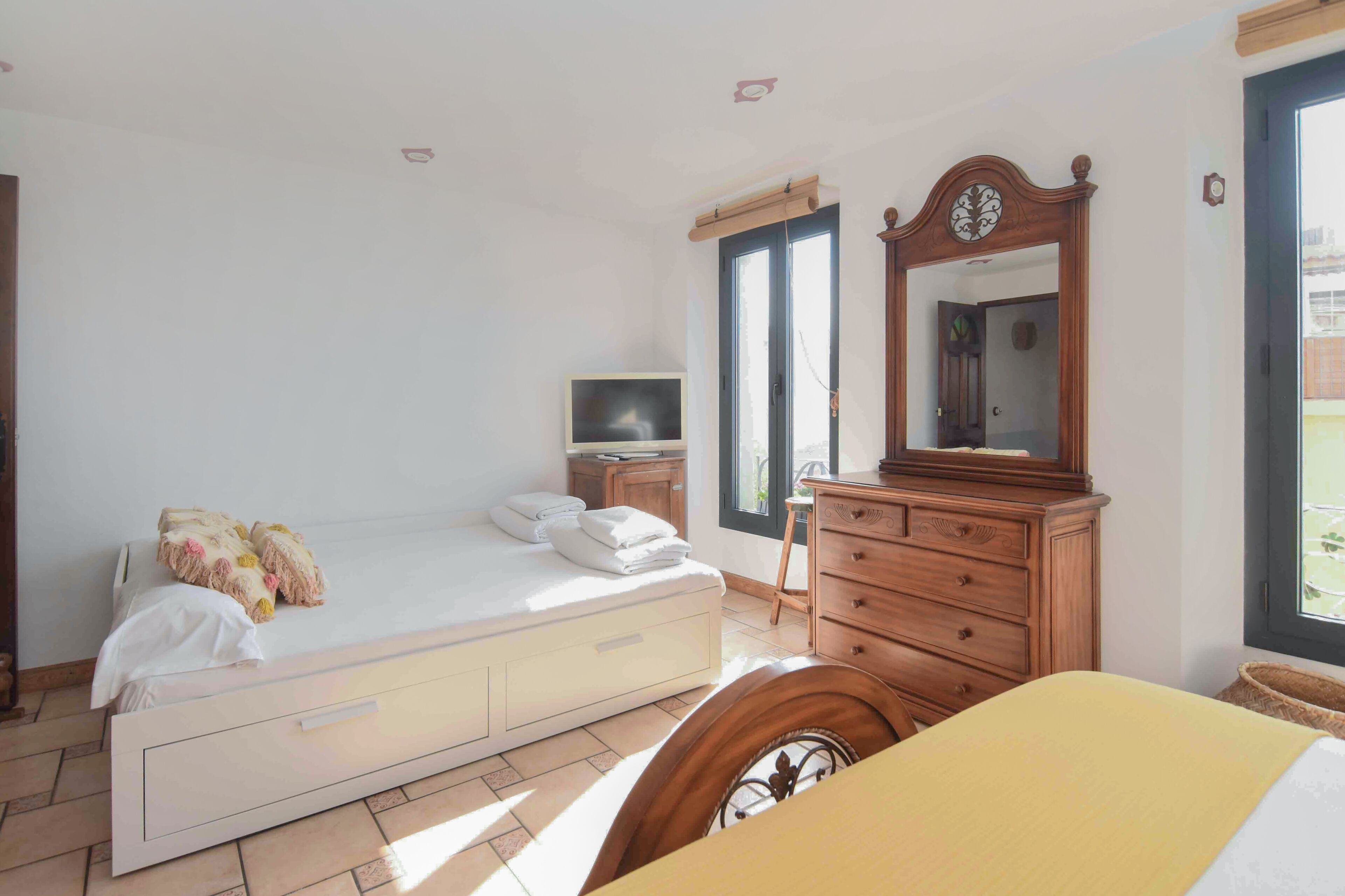 A bedroom with a bed, a dresser, a mirror, a television, and a window.