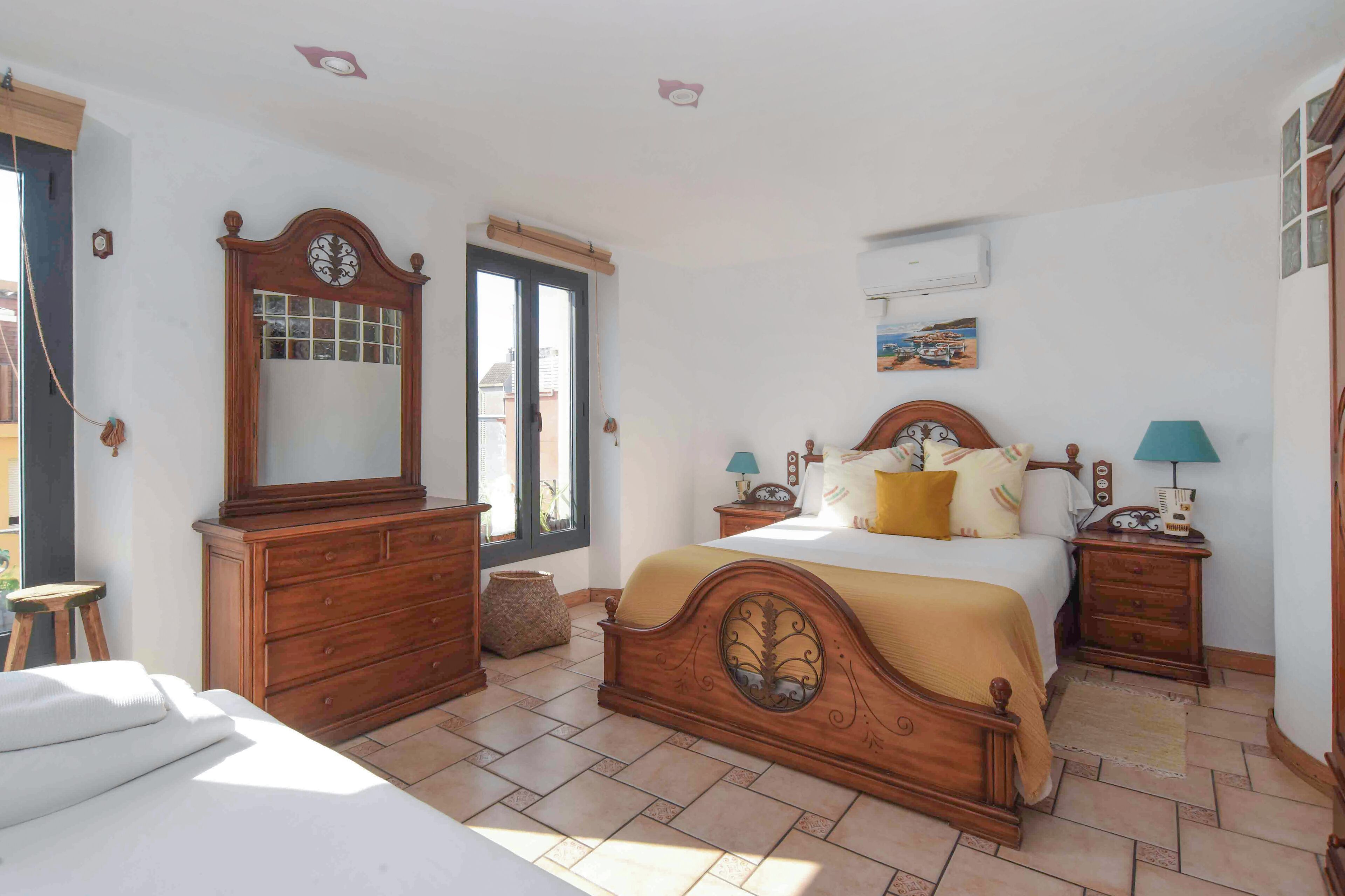 Un dormitorio con cama de madera, cómoda, espejo, ventana y un cuadro en la pared.