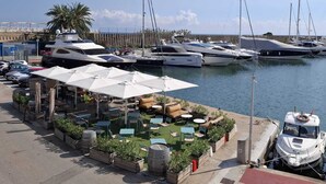 Un puerto deportivo con varios yates amarrados, mesas al aire libre con sombrillas y una vista despejada del agua.