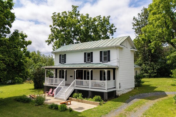 A two-story house with a porch, a covered front porch area, and a front yard with a bench and chairs.