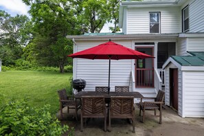 An outdoor patio with a table and chairs, a red umbrella, and a grill.