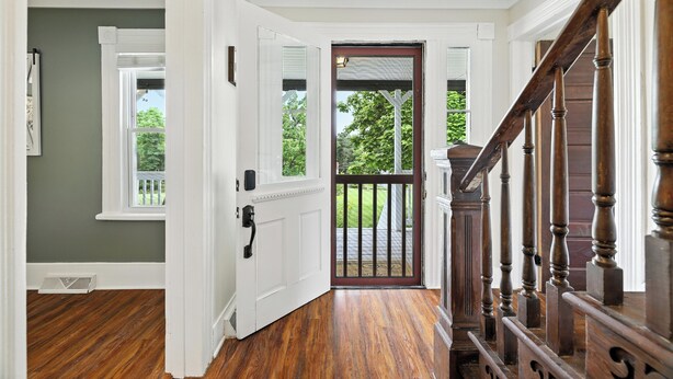 A hallway with wooden flooring, a white door, and a staircase with a wooden railing. - Super Cozy 5 Acre Farmhouse in Luray - Close to Everything (Luray)