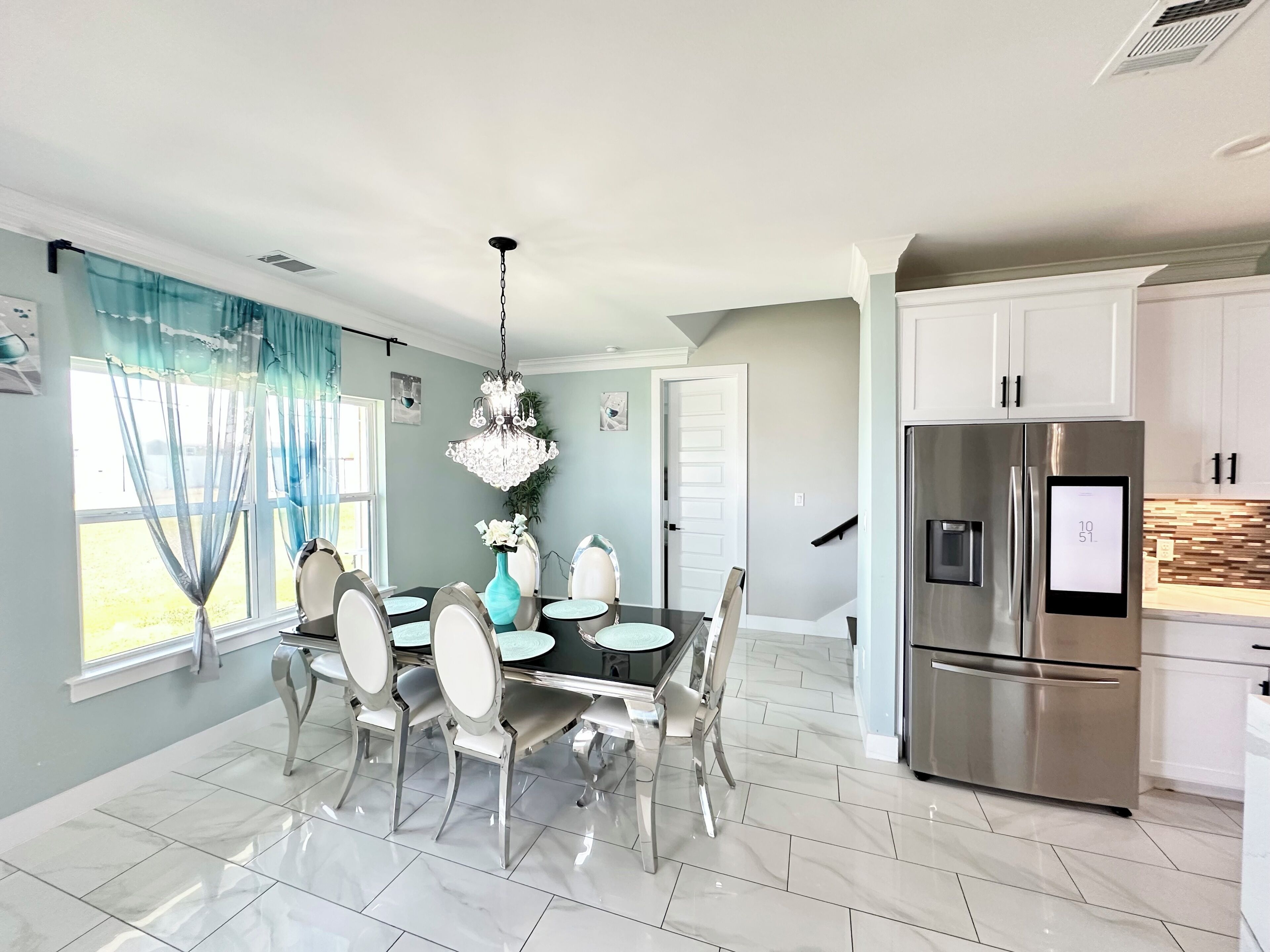 A modern kitchen with stainless steel appliances, a dining area with a chandelier, and a view through the window.